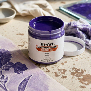 Encre de bloc Tri-Art Violet en pot ouvert avec pigment qui coule et échantillon de tissu floral